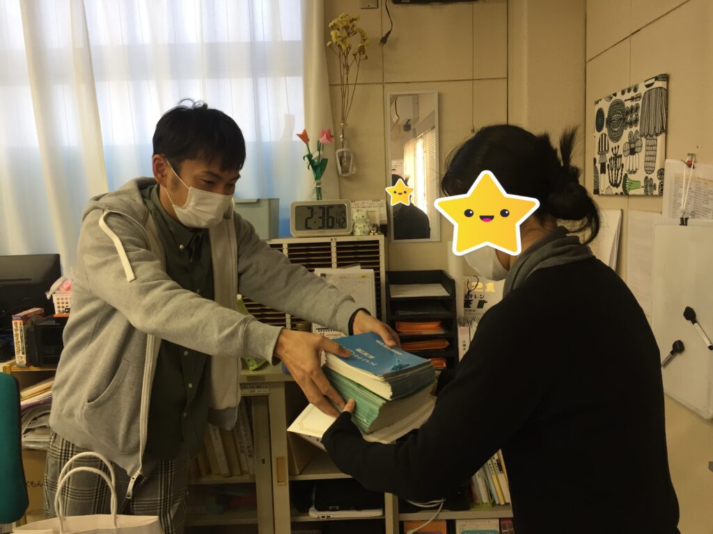 卒業までがんばった公文教材を社長からうけとるKさんの写真